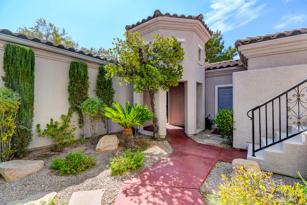 Walled entry courtyard with cypress, sago palms and a red concrete path