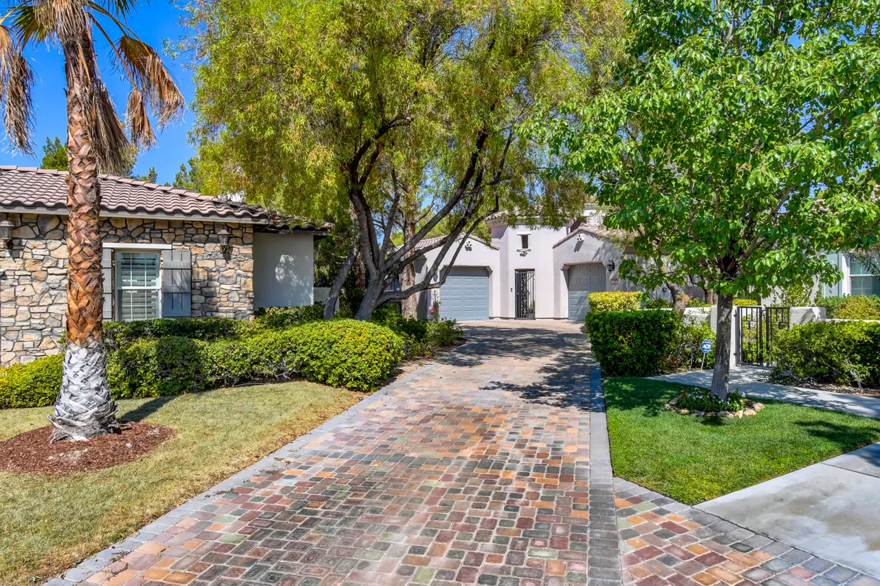 Long brick paver driveway approaching the home past a stone-clad neighbor and lawn