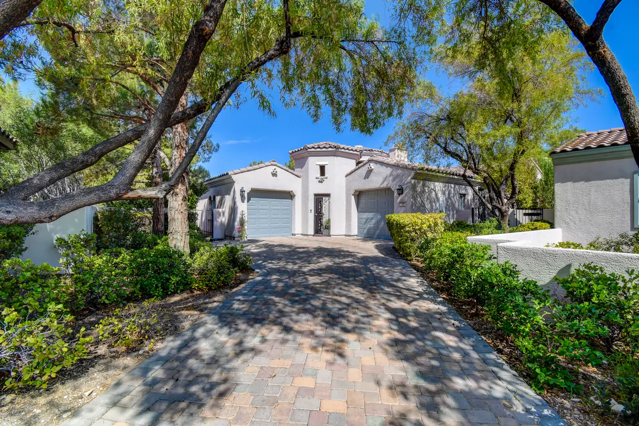 Paver driveway framed by mature trees leading to the stucco villa and its two garages