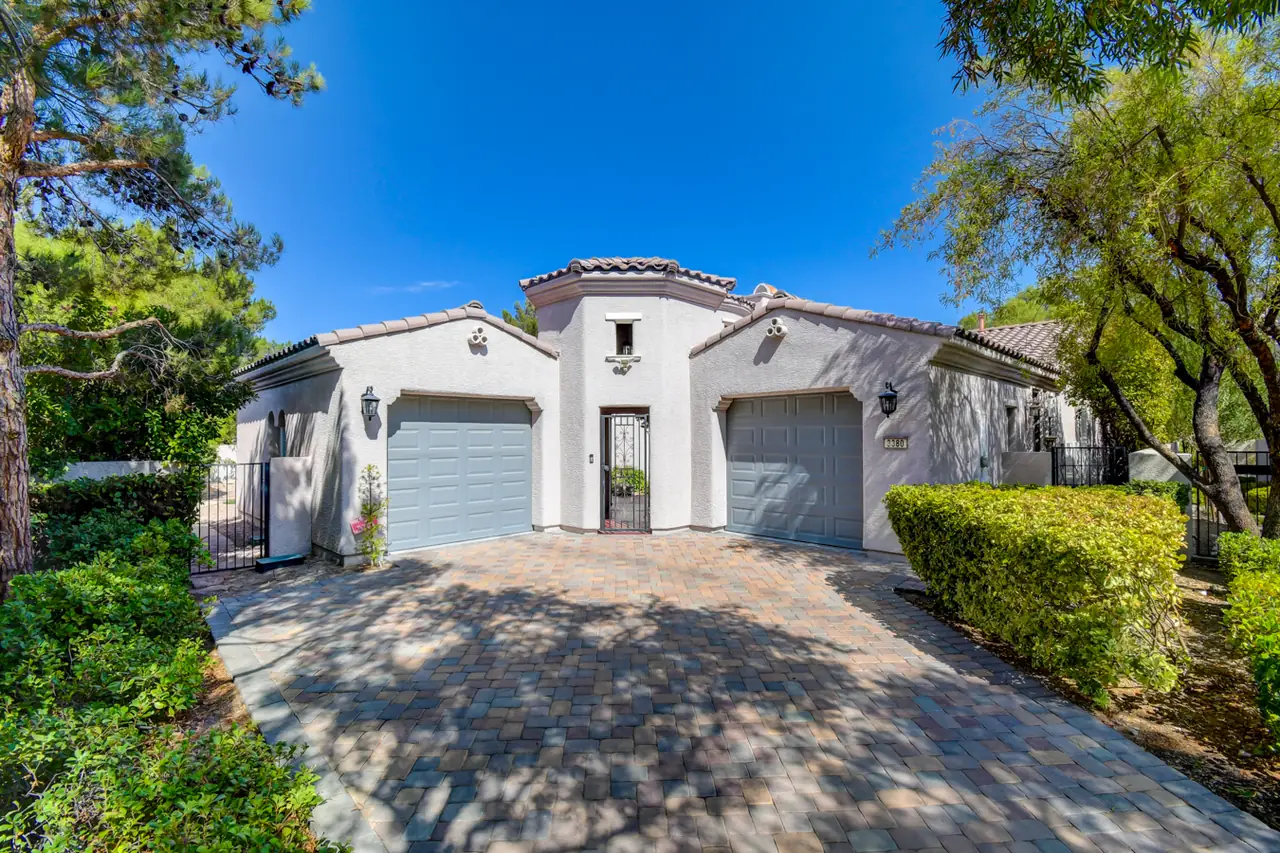Front of the Tuscan-style villa with an arched center entry between two garages, under mature trees