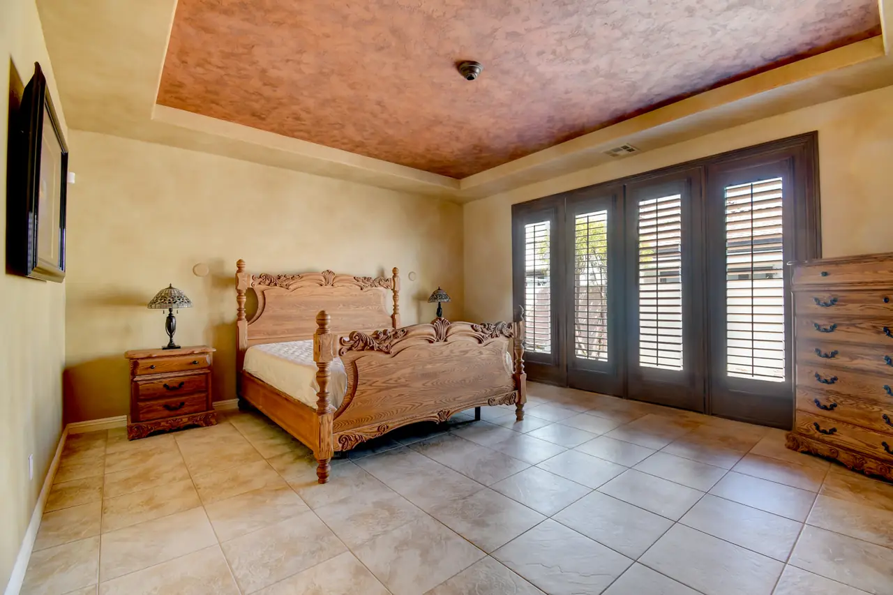 Primary bedroom with textured tray ceiling and a wall of shuttered French doors